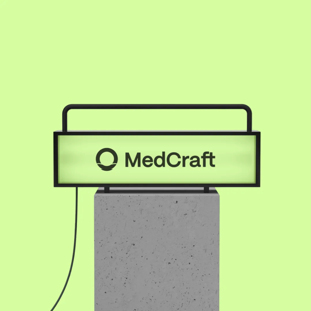 A MedCraft lightbox sign glowing on a concrete plinth against Reef green